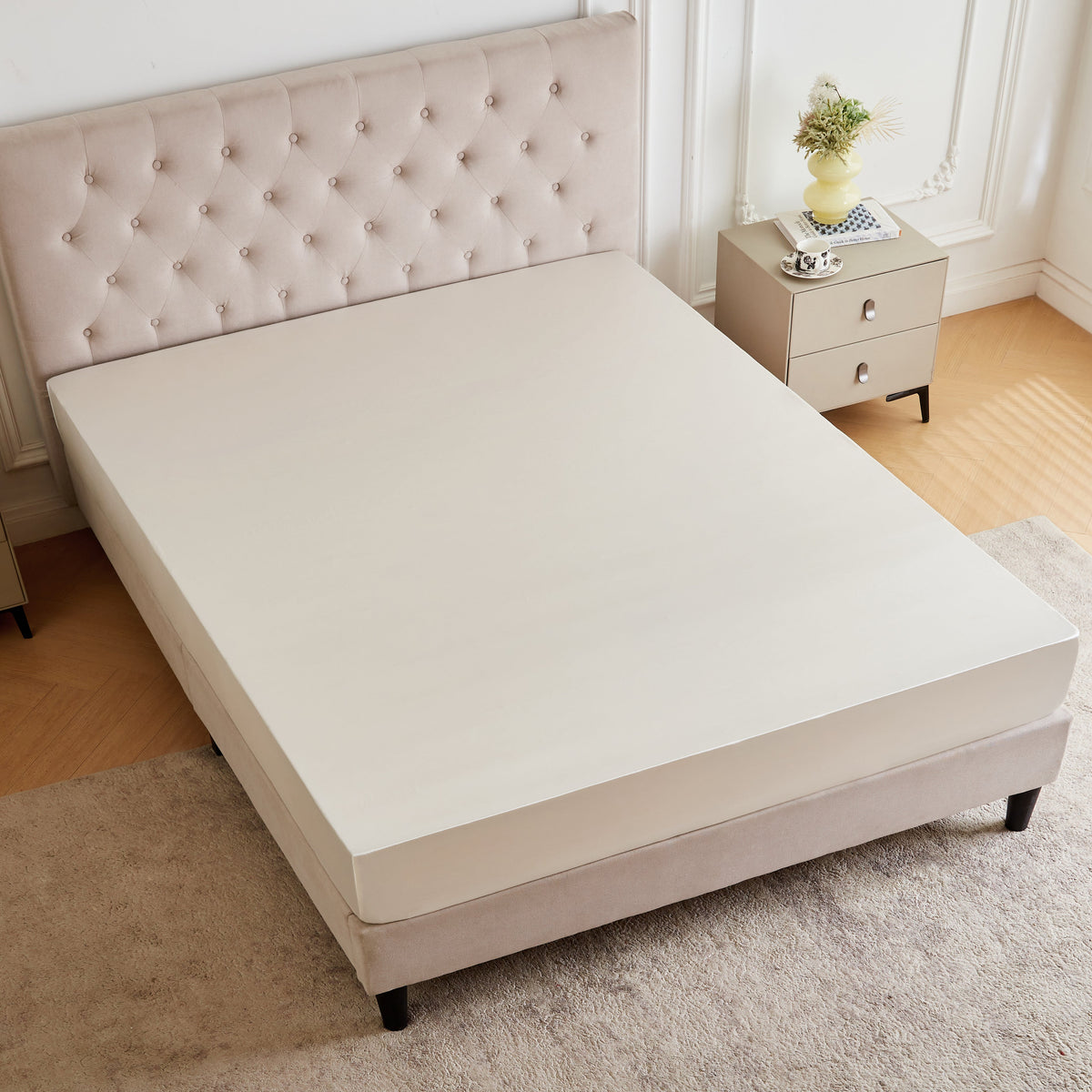 A beige upholstered bed with a tufted headboard, dressed in a 30 Momme Silk Fitted Sheet, beside two nightstands.