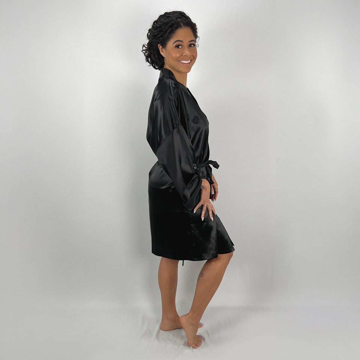 A woman in a side view, gracefully posing in a relaxed-fit black silk robe