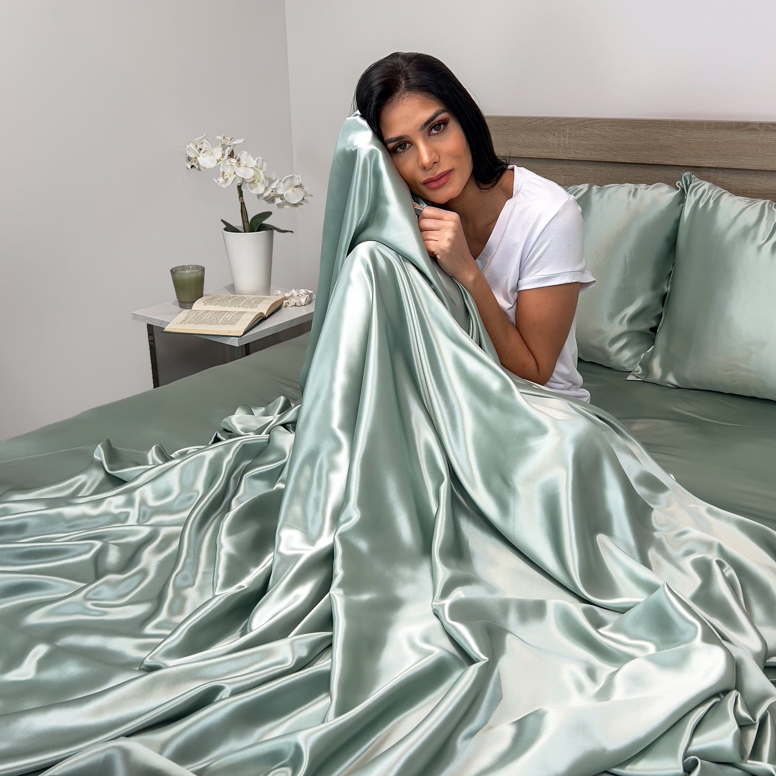 Sage silk flat sheet draped over a neatly made bed in a bright, modern bedroom