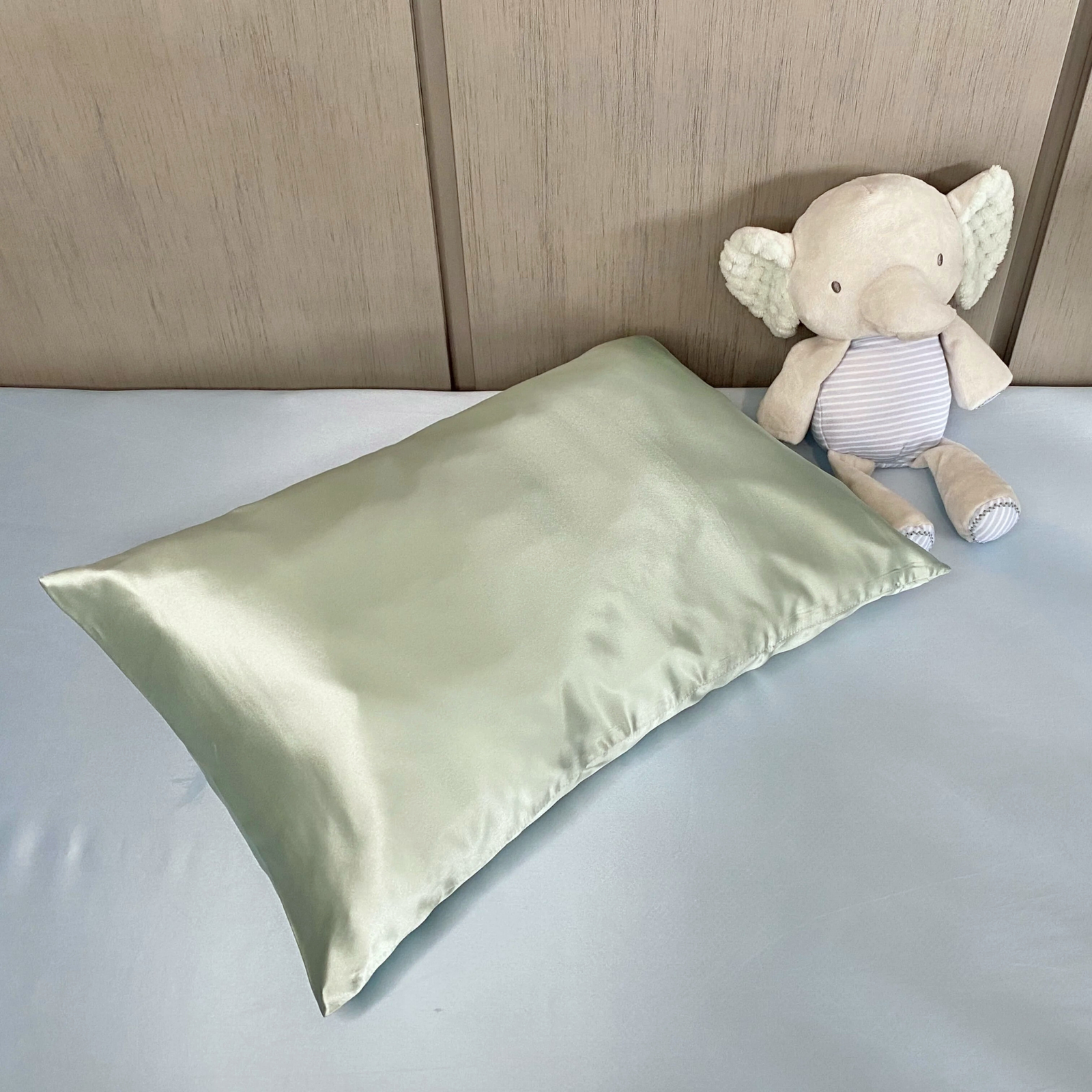 A light brown teddy bear sits next to the Pure Silk Toddler Pillowcase in Goodnight Green on a white background.
