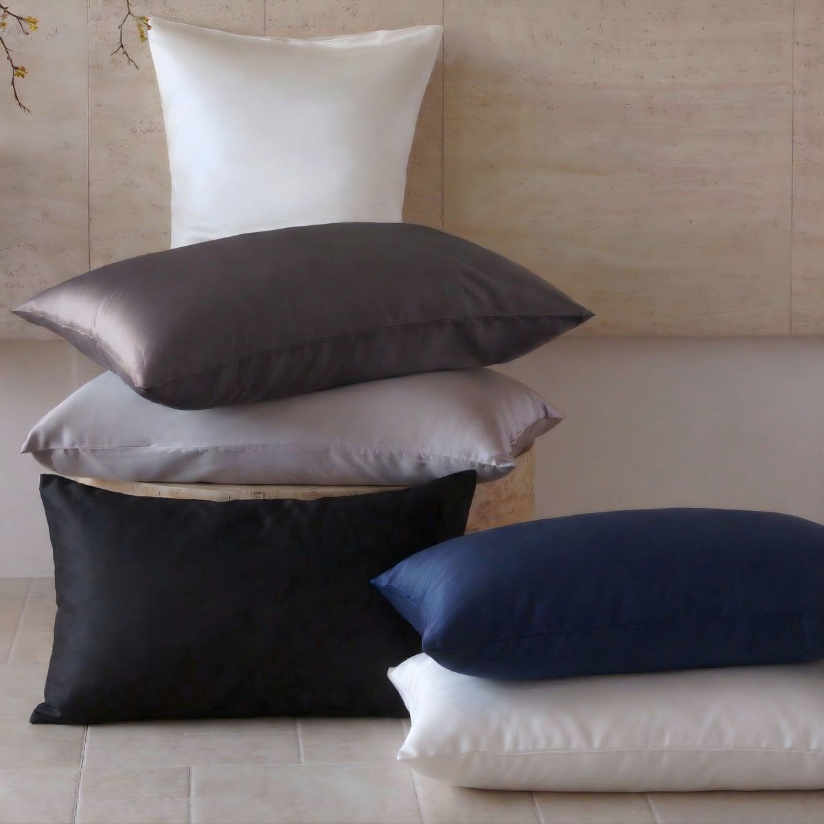 A stack of 30 momme silk pillows in white, gray, and blue is shown against a neutral wall.