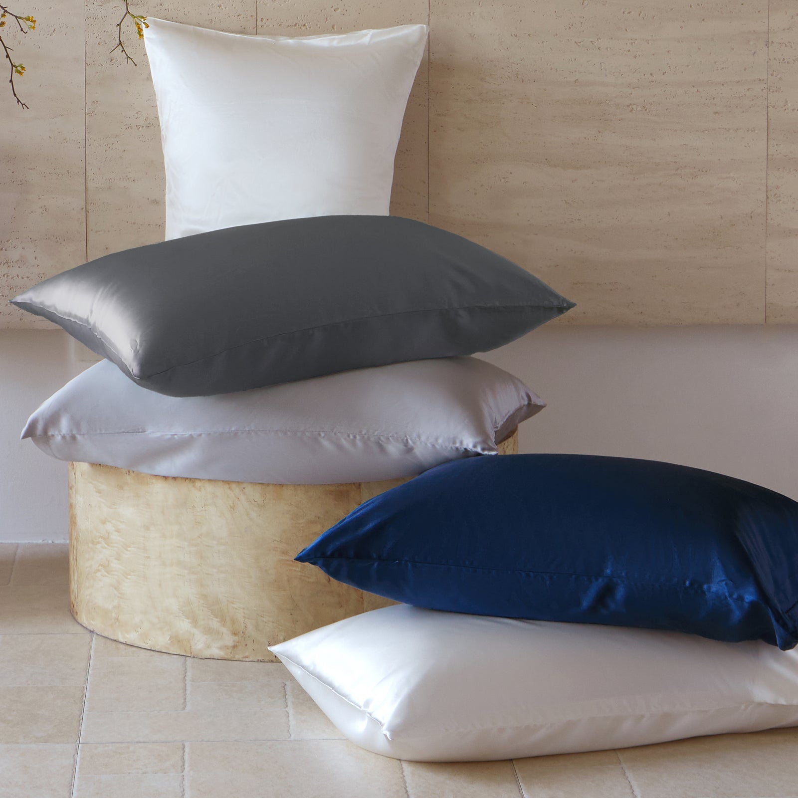 A stack of 30 momme silk pillows in white, gray, and blue is shown against a neutral wall.