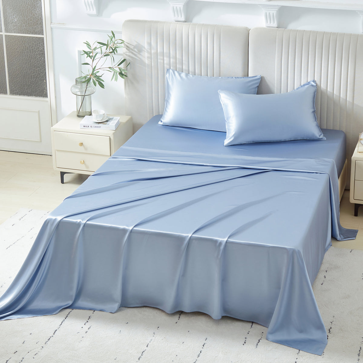 A neatly made bed with light blue silk sheets and two matching pillows in a bright, modern bedroom.