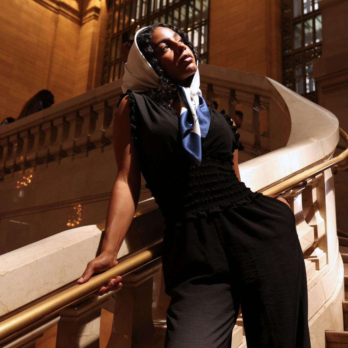 Woman on marble staircase wearing Mulberry Park Silks' Silk Square Head Scarf in Navy/Ivory, styled elegantly with a black jumpsuit.