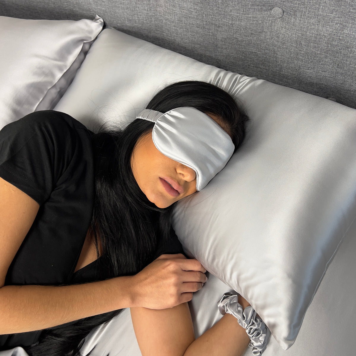Mulberry Park Silks pillowcase and sleep mask gift set with woman resting on silver silk bedding.