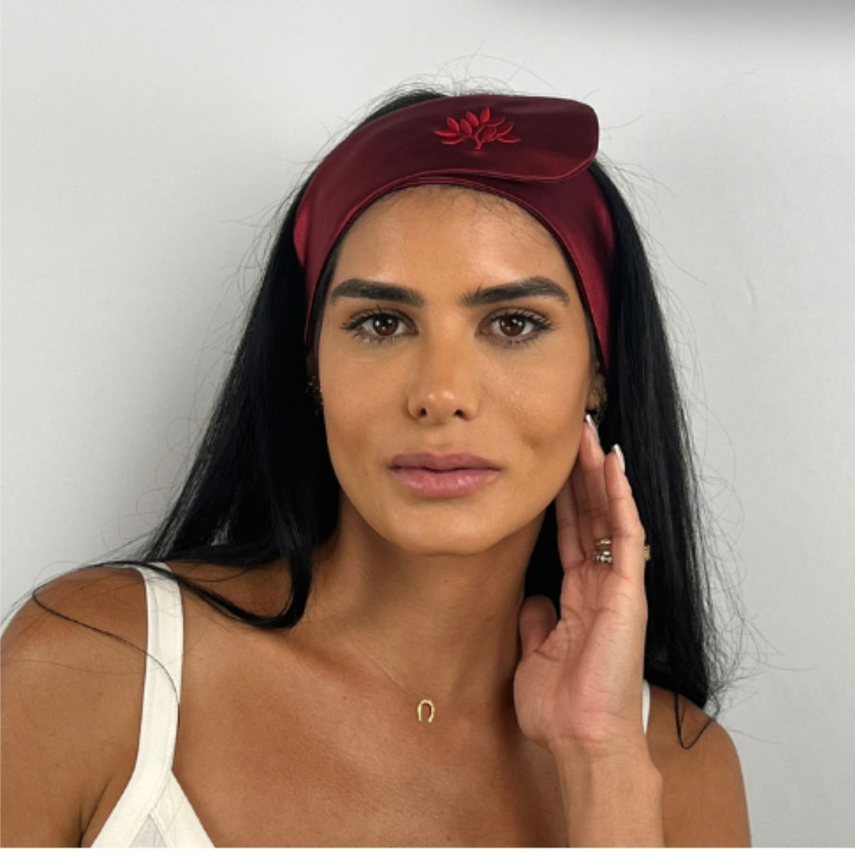 Woman with long black hair wears a Mulberry silk headband and white top, posing in front of a plain background.