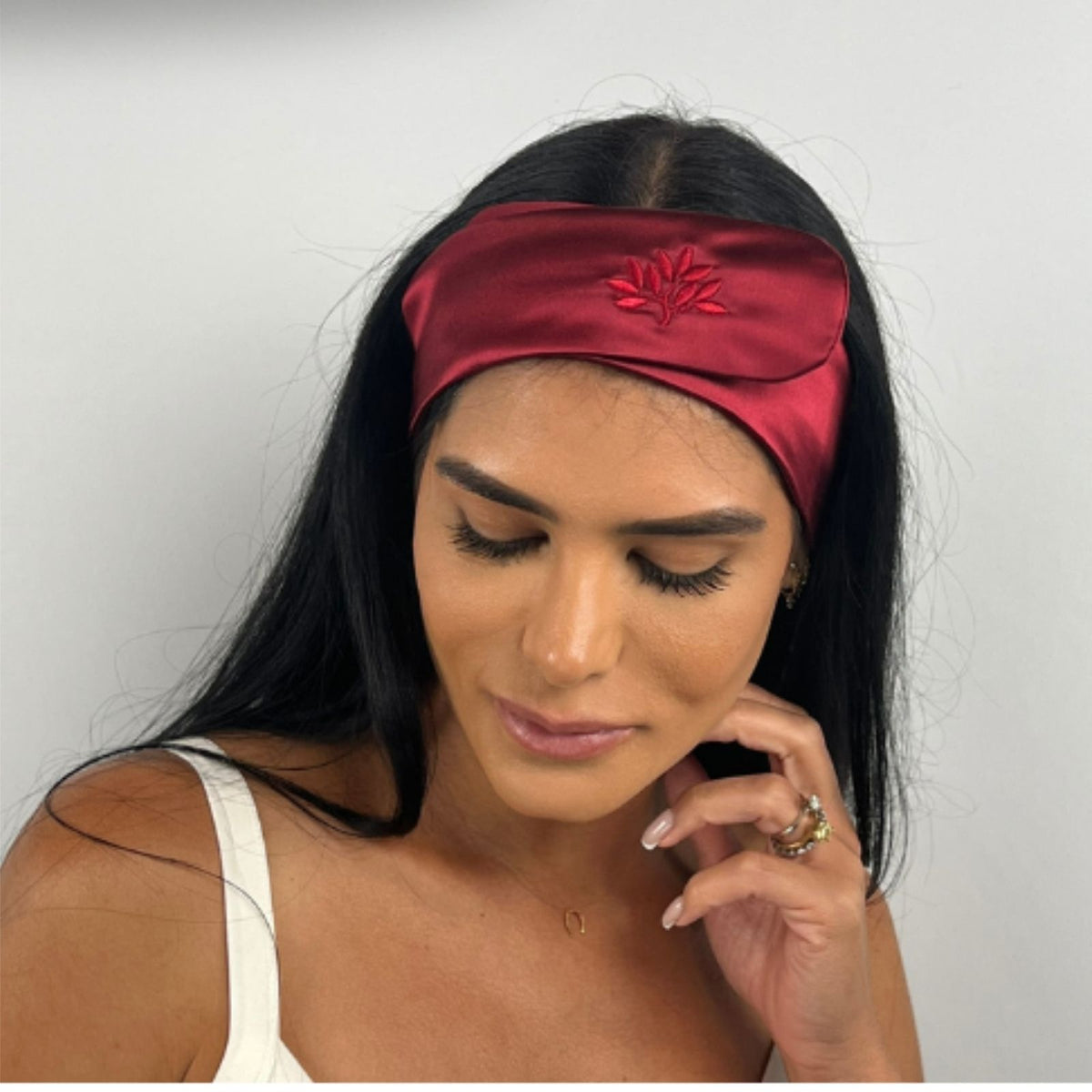 Woman with long dark hair wears a Mulberry silk headband and white top, looking down with a neutral expression.